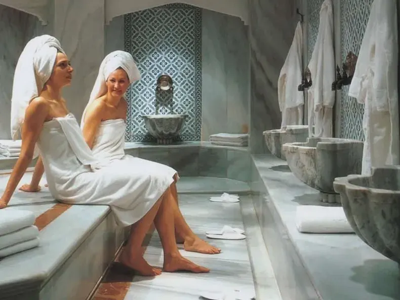 After the bath, two guests wrapped in towels take a rest by the marble basins